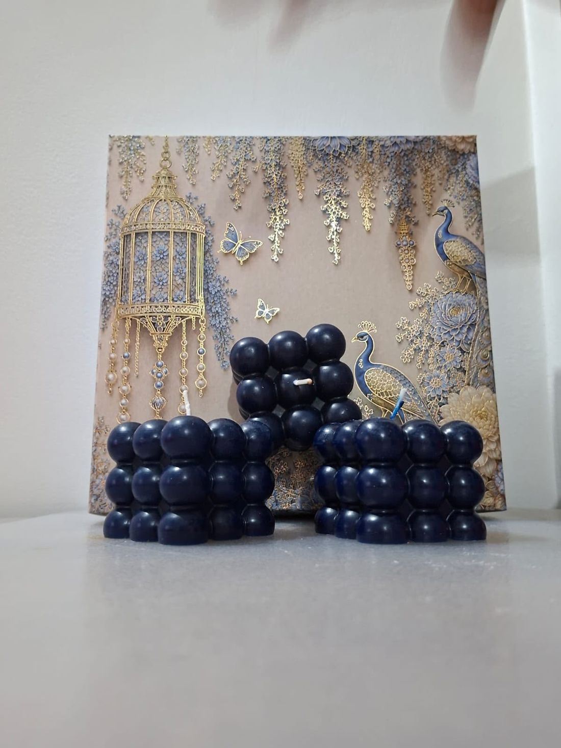Three midnight-navy bubble candles in front of a peacock-print gift box