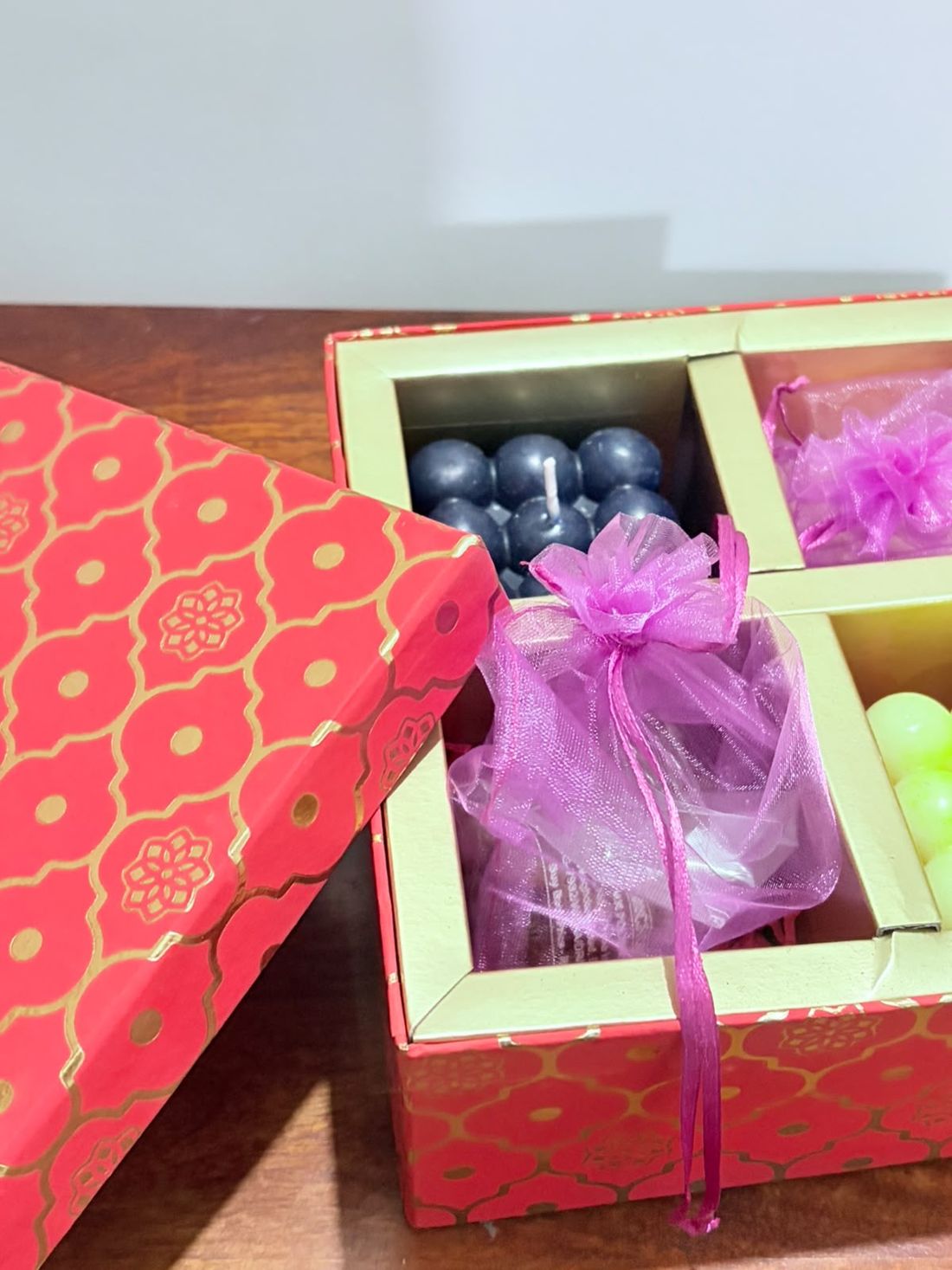 Open red and gold gift box with navy bubble candles and organza pouches